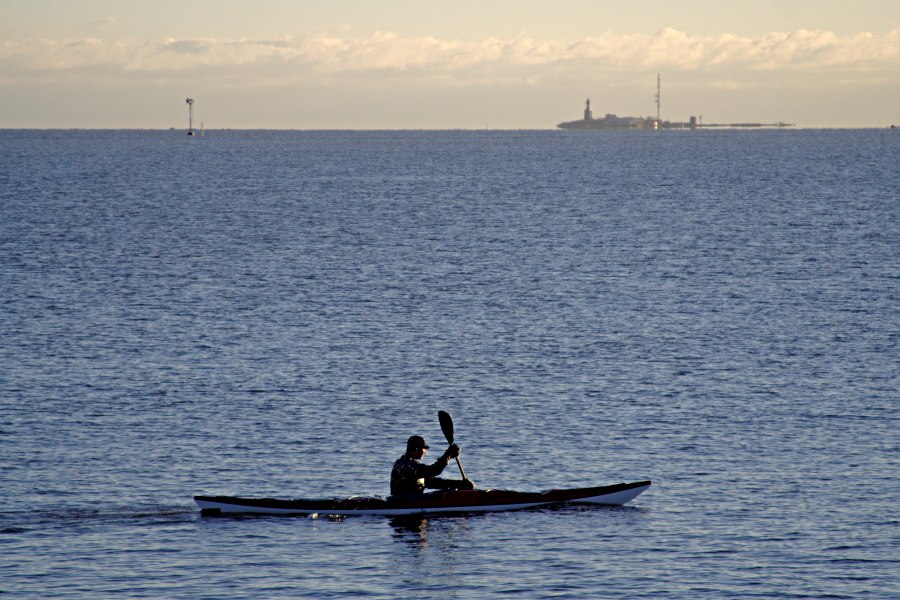 A paddler passes Uunisaari island, Harmaja light house in the background